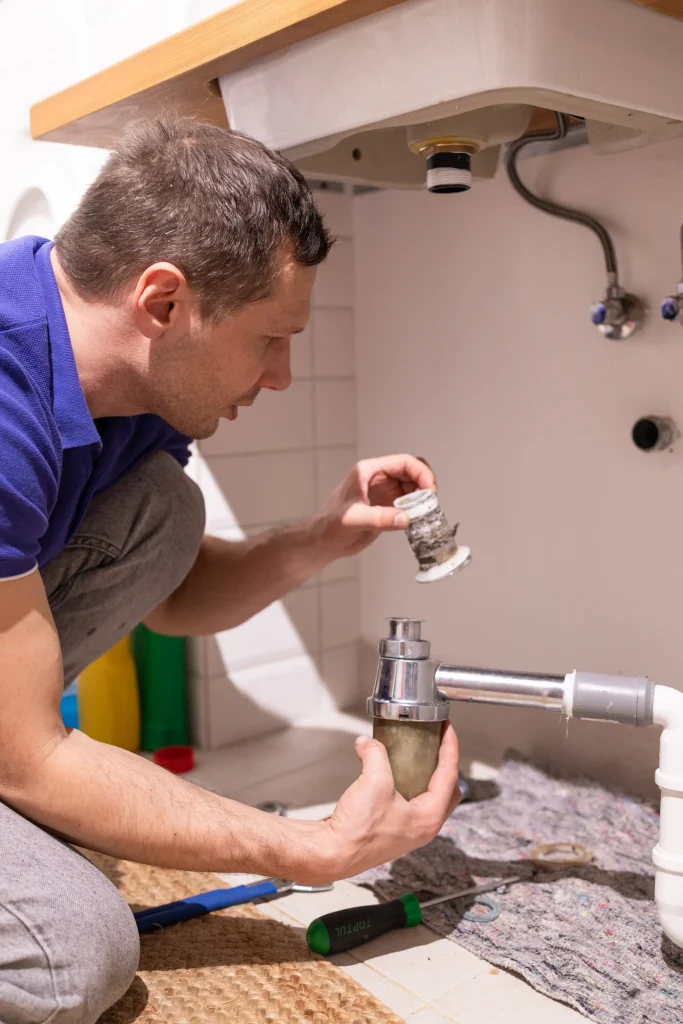 A plumber fixing a broken pipe under a sink.