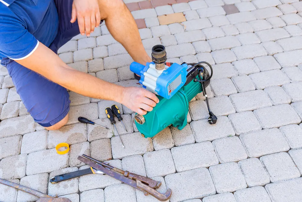 A plumber fixing a water pump with wrenches and screwdrivers.