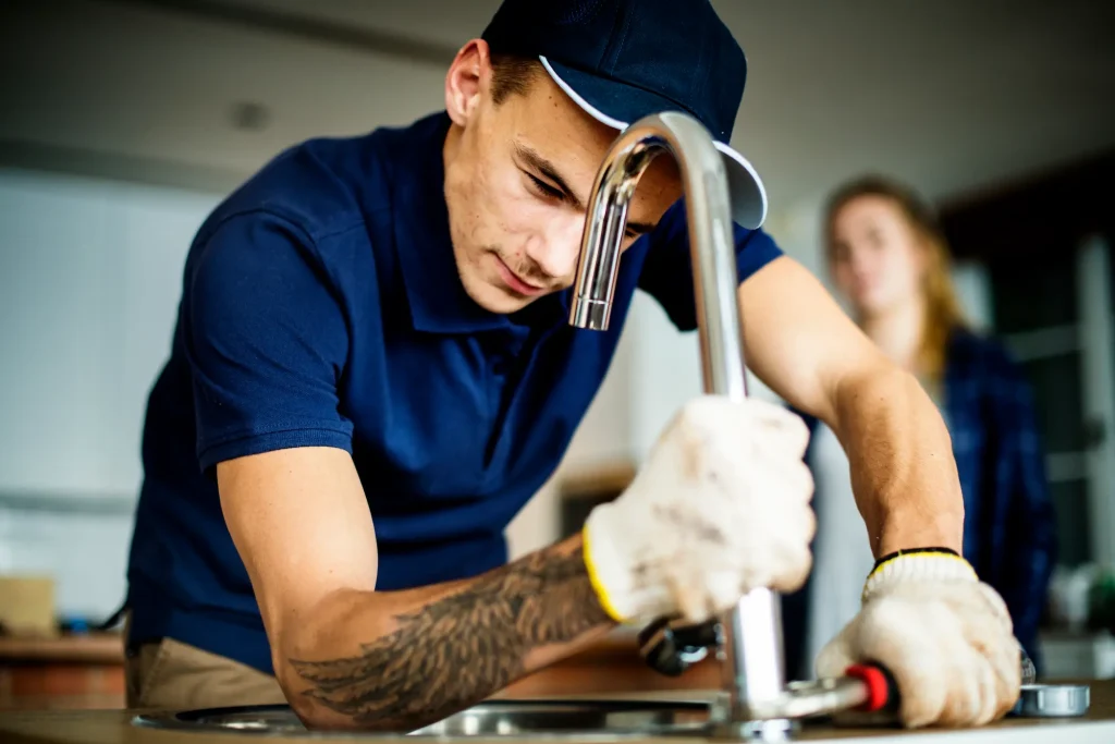 A plumber works on a leaky kitchen faucet.
