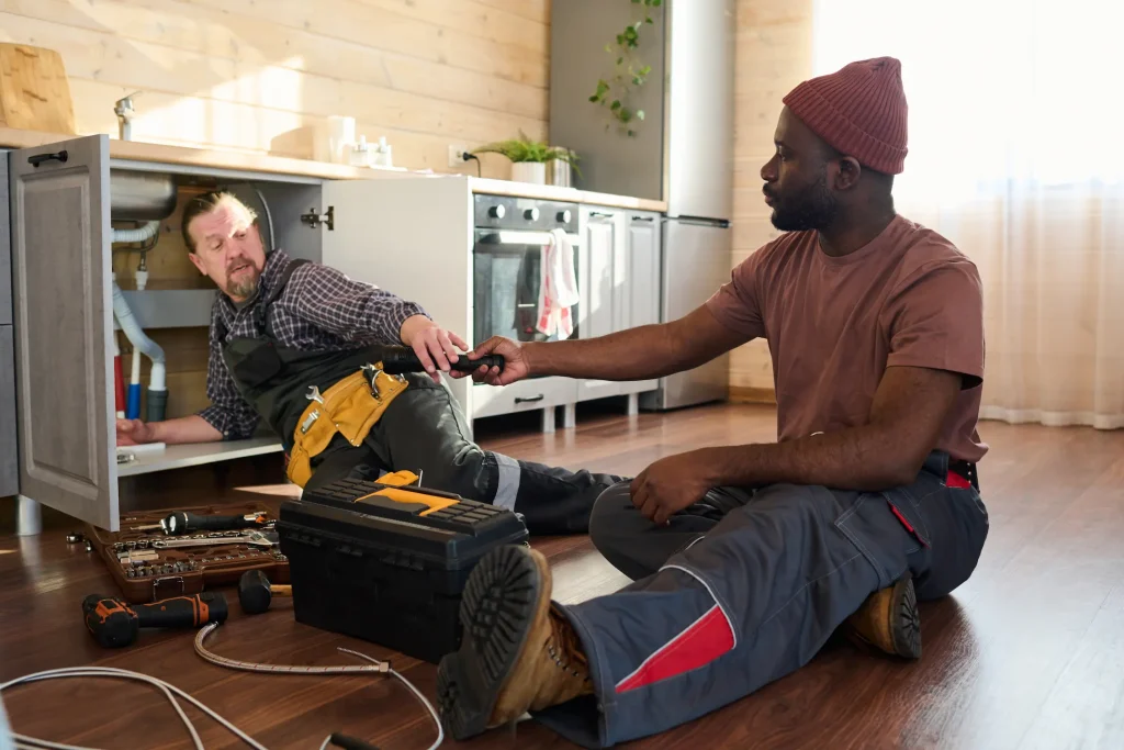 Two plumbers working under a kitchen sink.